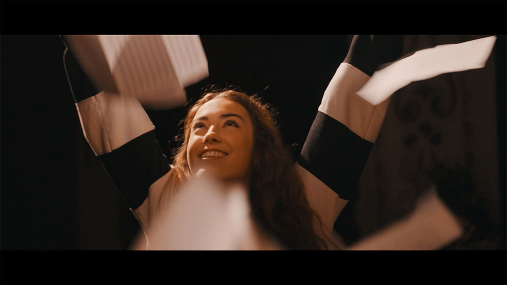 Chica sonriente con los brazo en alto y papeles cayendo a su alrededor